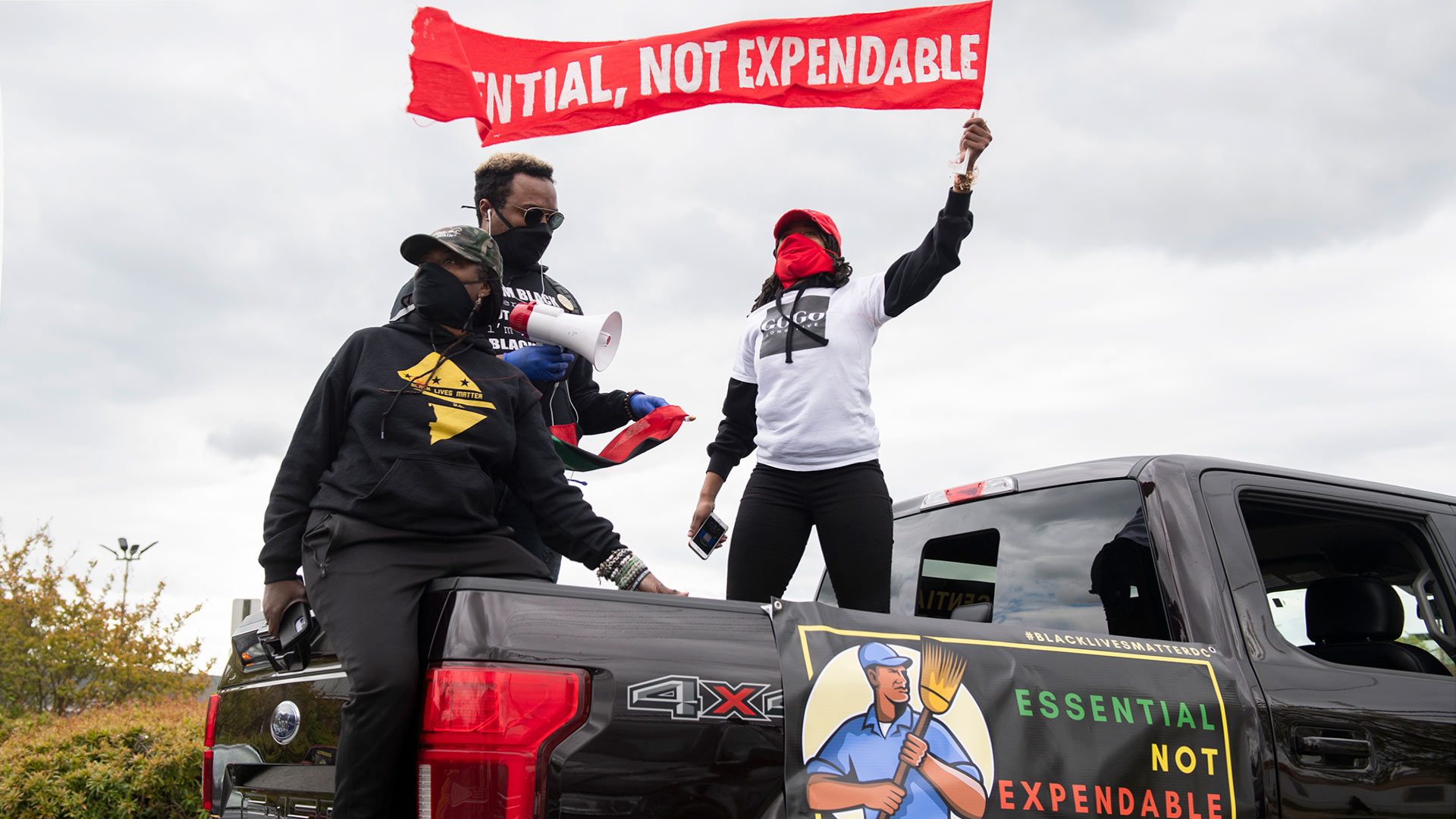 People standing on a truck waving sign saying essential, not expendable