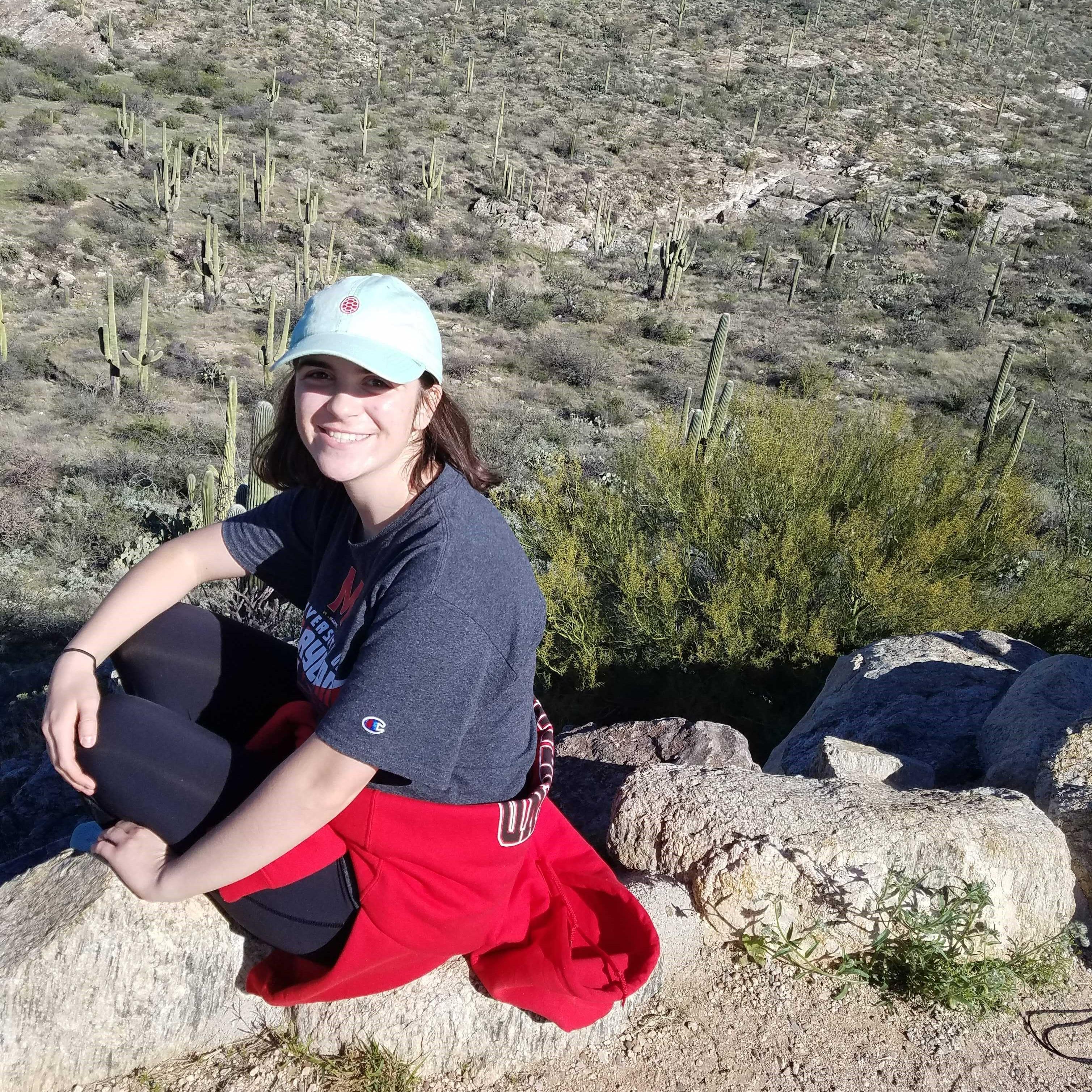 Cameron Smith smiles, sitting on rocks with a field of cacti behind her.